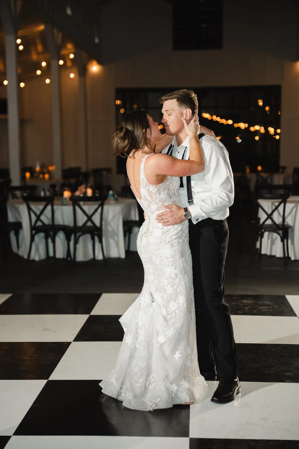 Bride and groom sharing an intimate last dance on black and white checkered dance floor at Tampa Bay wedding reception with string lights